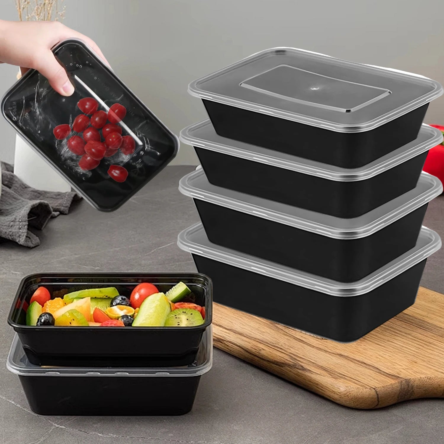 Set of black food containers with clear lids on a gray surface, one container is opened to reveal fruit.