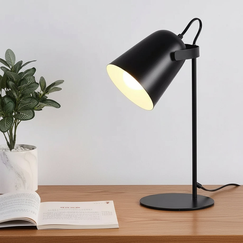 Black table lamp on a white surface with a plant and book in the background
