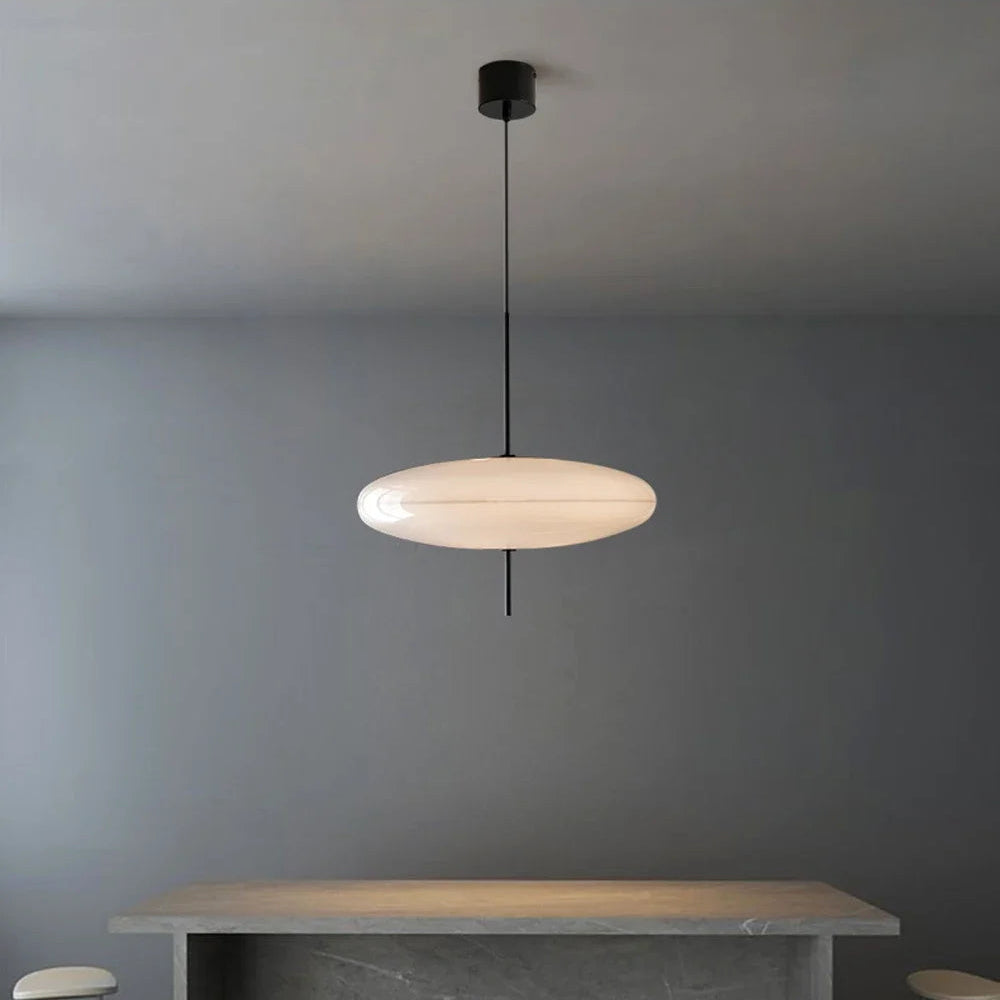 Modern pendant light hanging above a dining table with stools in a minimalistic setting.