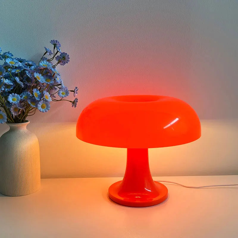 Orange mushroom table lamp on a white surface with a vase of flowers next to it.