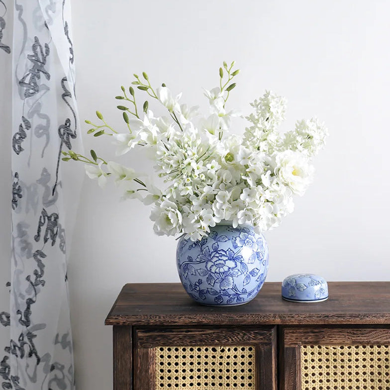 Floral arrangement in a blue and white vase on a wooden cabinet with a white wall background.
