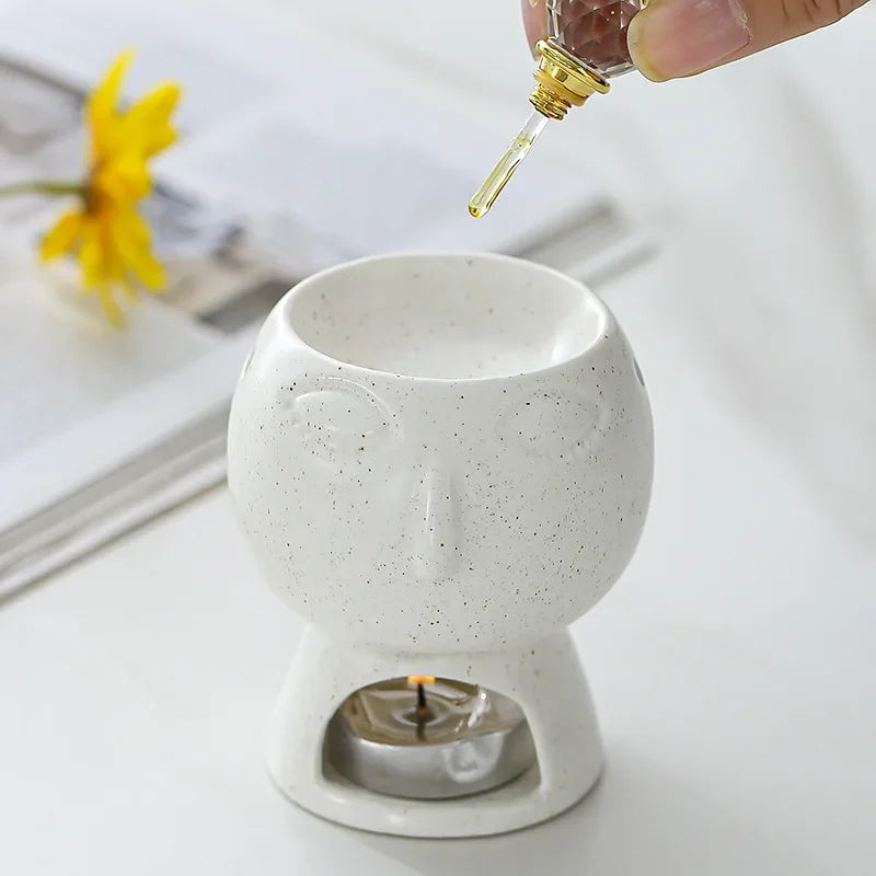 White ceramic oil burner with a hand pouring oil into it on a light background.