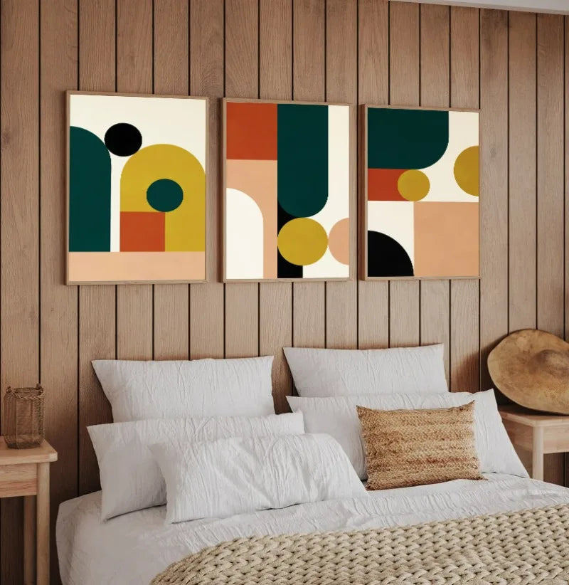 Three abstract art pieces on a wooden wall above a bed with white bedding and a woven headboard.