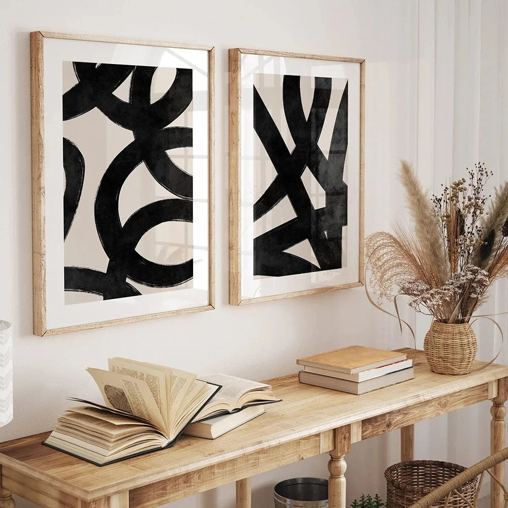 Two abstract art pieces on a wall above a wooden console table with books and a vase.