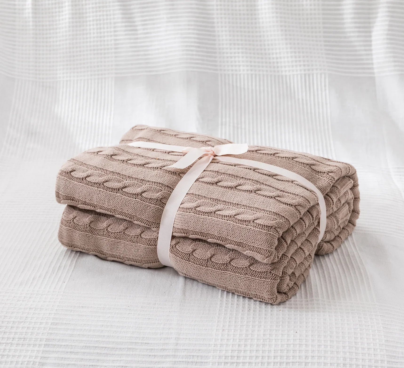 Folded beige blanket tied with a ribbon on a white textured background