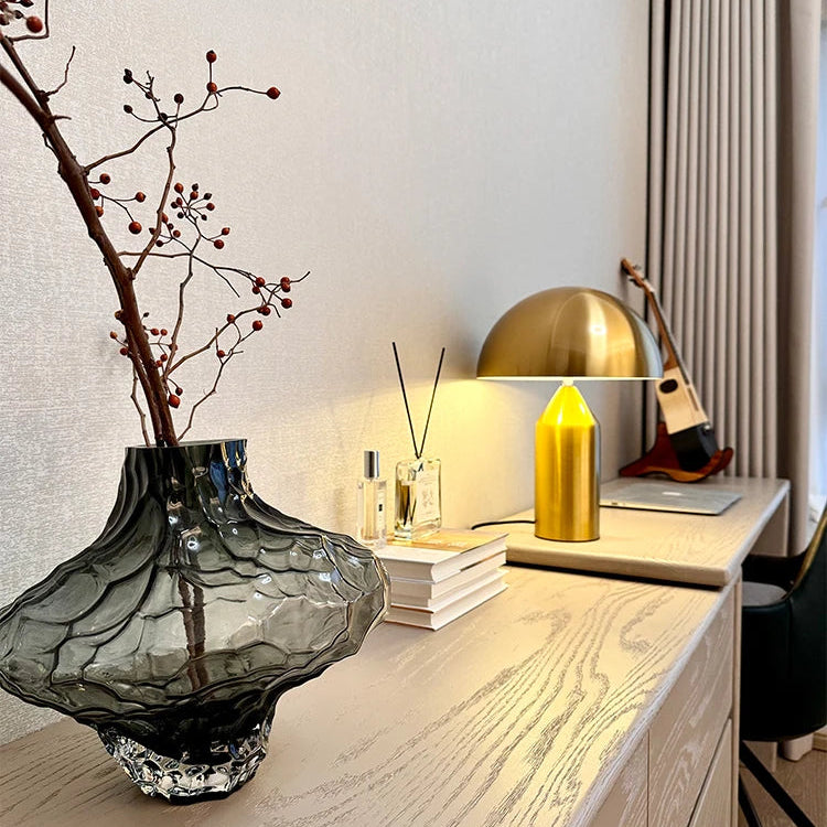Modern office desk with decorative elements including a glass vase, gold lamp, and books.