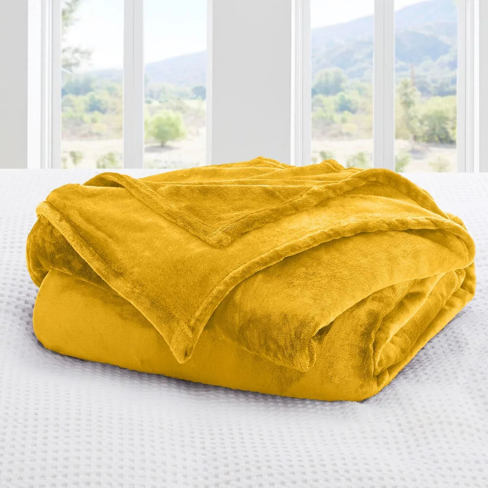 A mustard gold blanket on a bed with a window view of trees and mountains