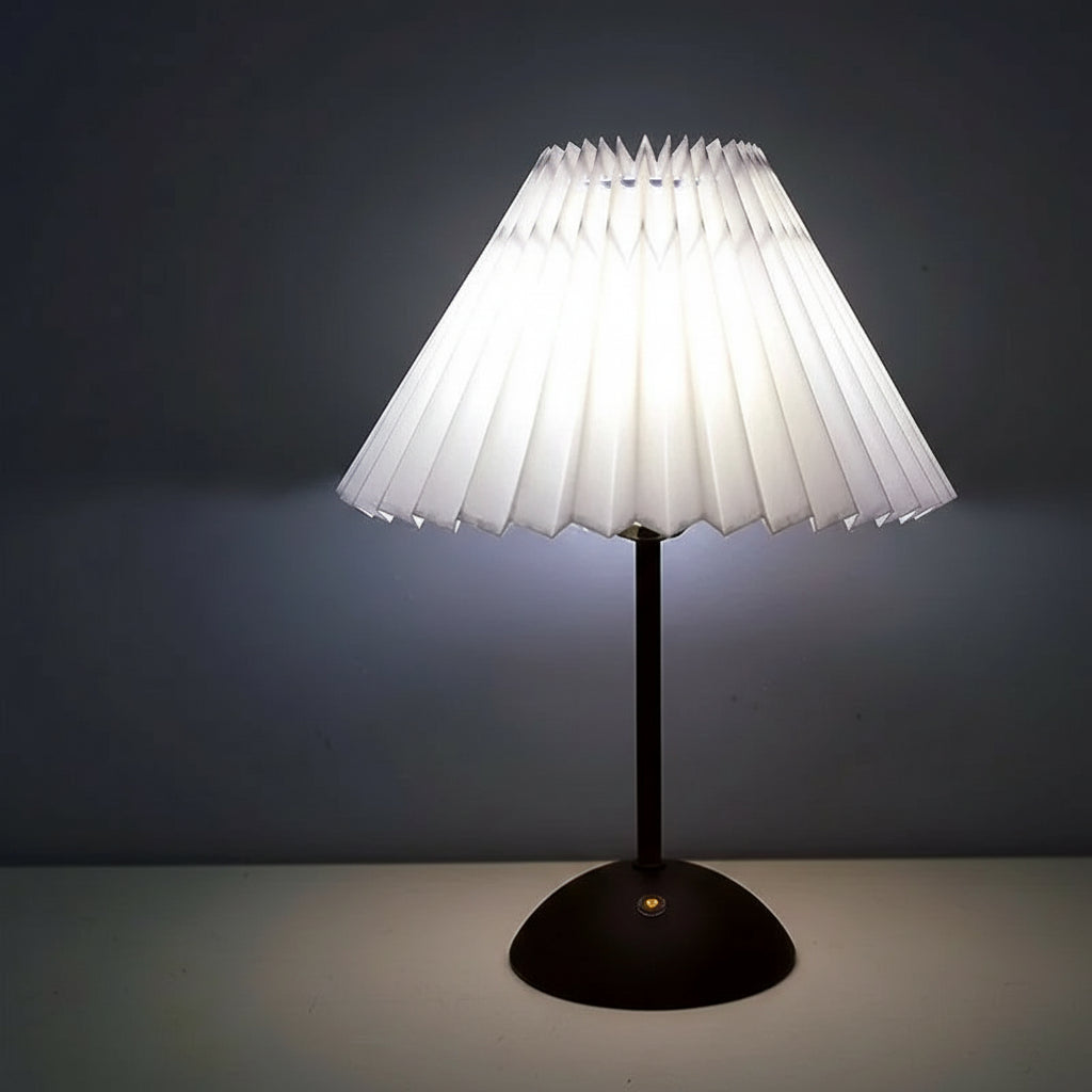 Table lamp with a pleated white shade and a black base on a dark background.