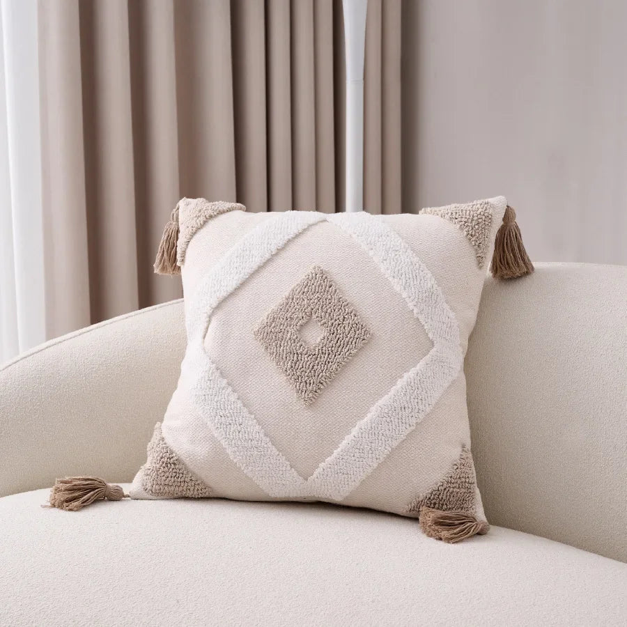 Decorative pillow with tassels on a beige sofa against a neutral background