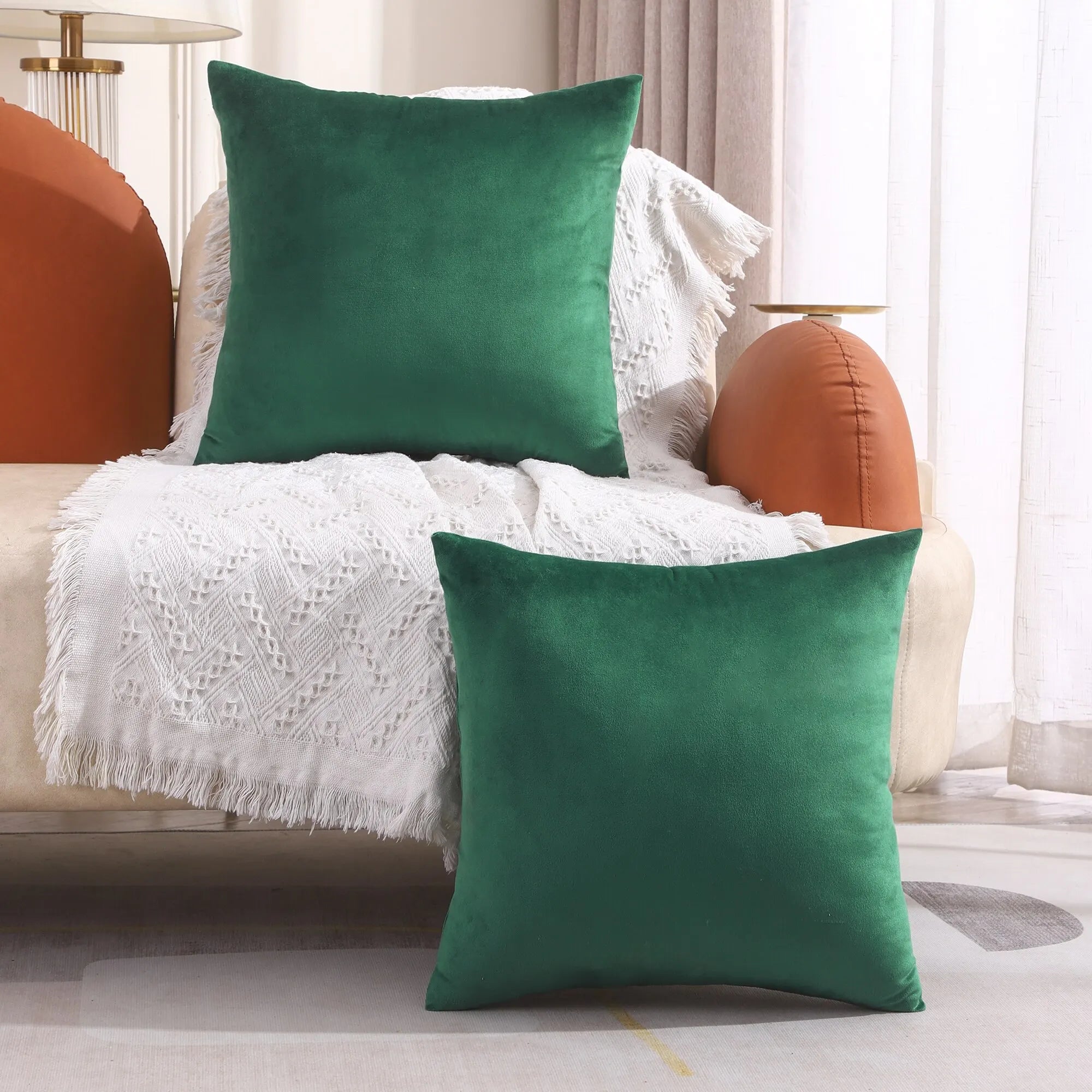 Two green pillows on a beige sofa with a white blanket and orange cushions.