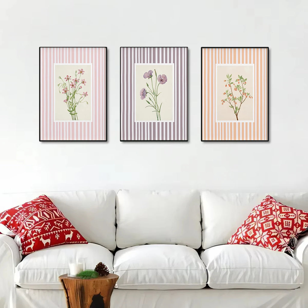 Three framed botanical prints above a white sofa with red patterned pillows.