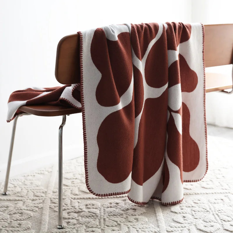 Rust and cream abstract jacquard blanket with blanket stitch edge draped over a wooden chair on a textured cream rug