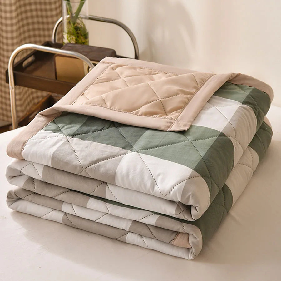 Sage green, grey, and white block check quilted comforter with a beige border, folded on a bed