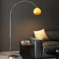 Mushroom-shaped Bauhaus floor lamp with arched metal frame and amber glass shade beside a black leather sofa