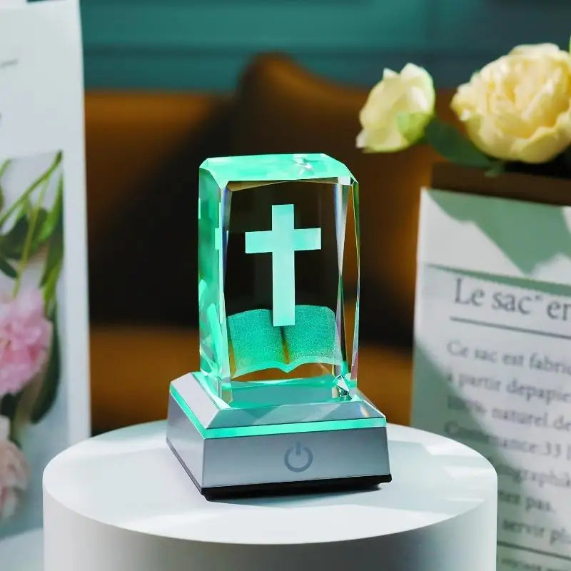 Crystal object with a cross on a white pedestal against a blurred background with flowers.