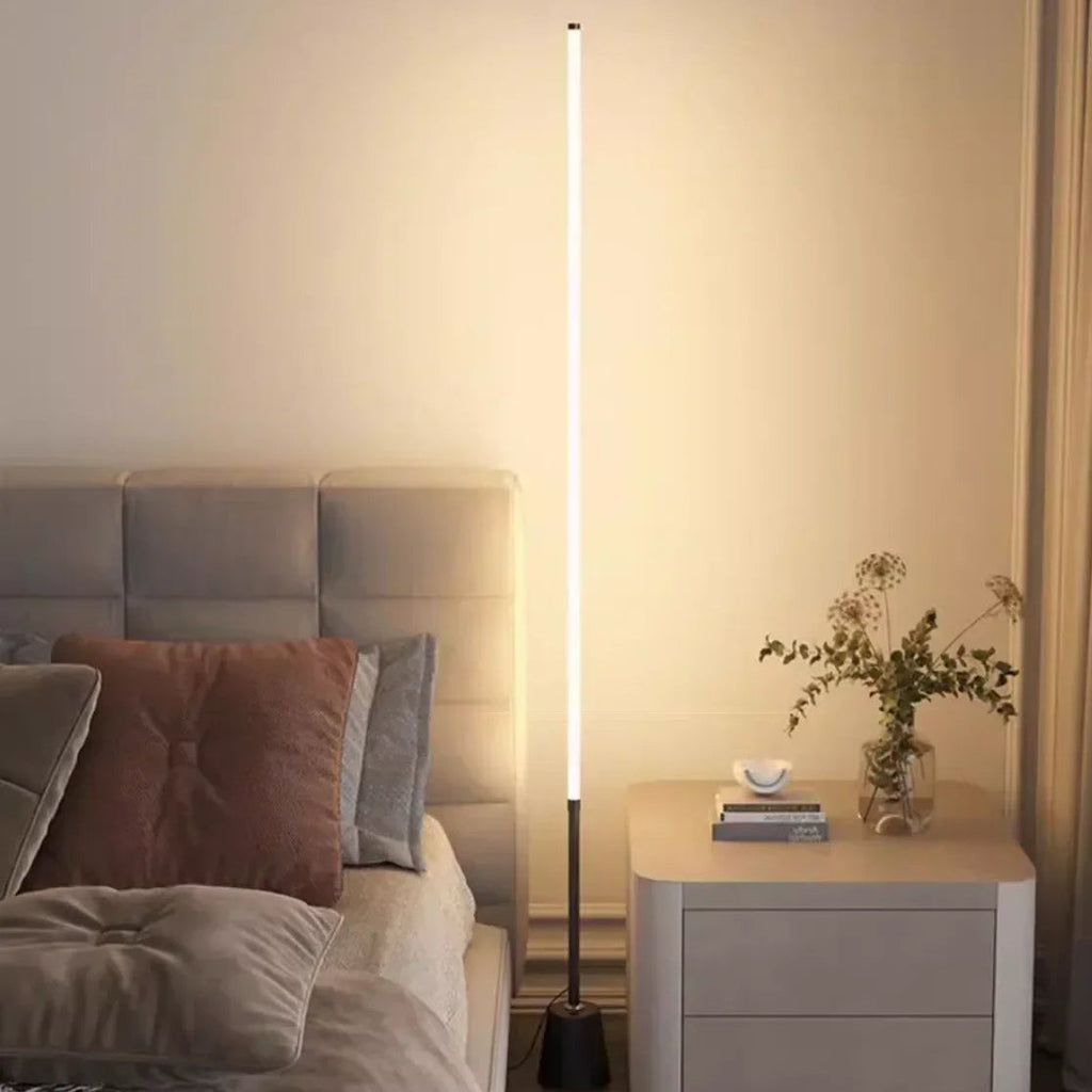 White vertical LED floor lamp beside a modern bed