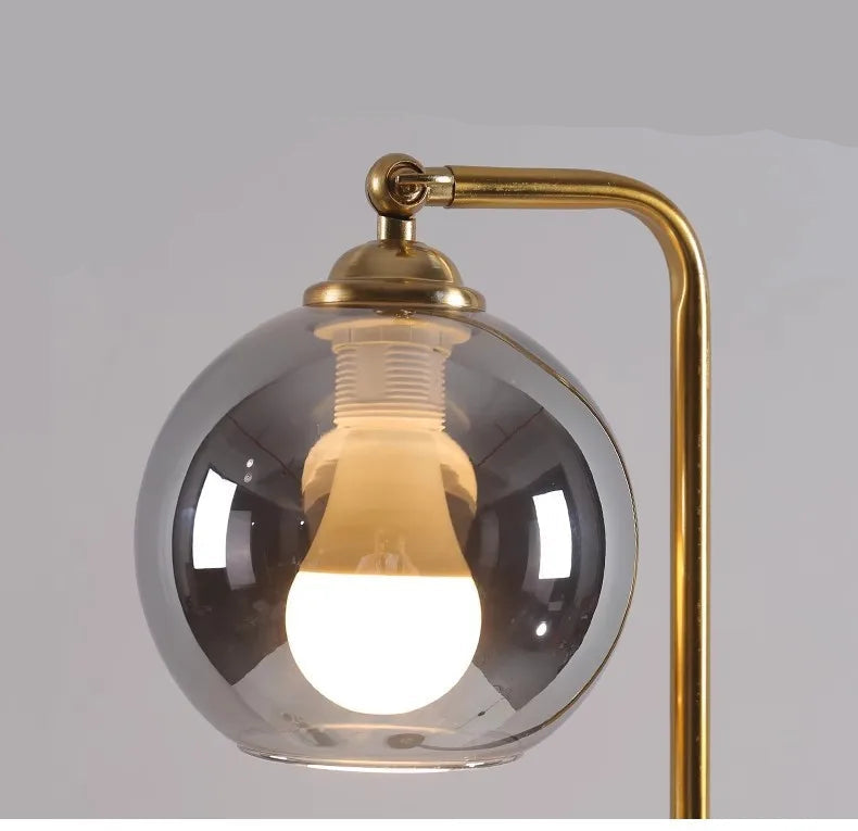 Modern black and brass floor lamp with clear glass globe shade beside a white side table