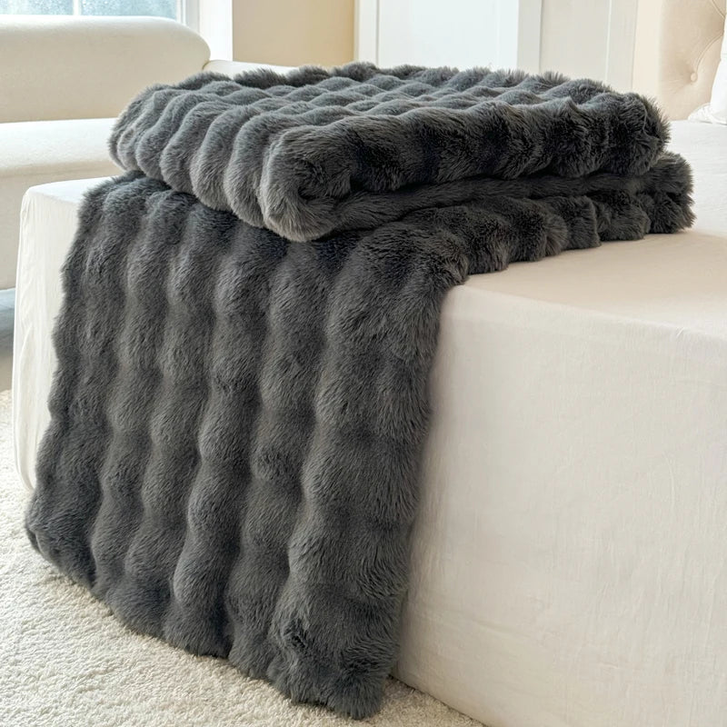 A faux-fur charcoal blanket draped over a white sofa.