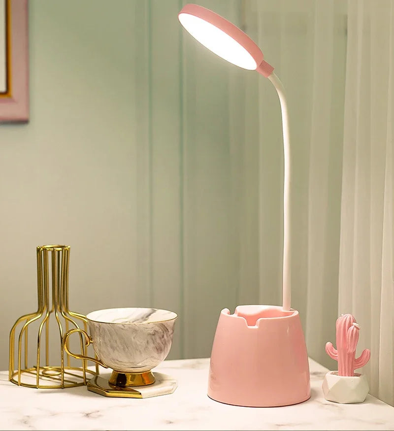 Pink desk lamp on a surface with decorative items against a neutral wall.