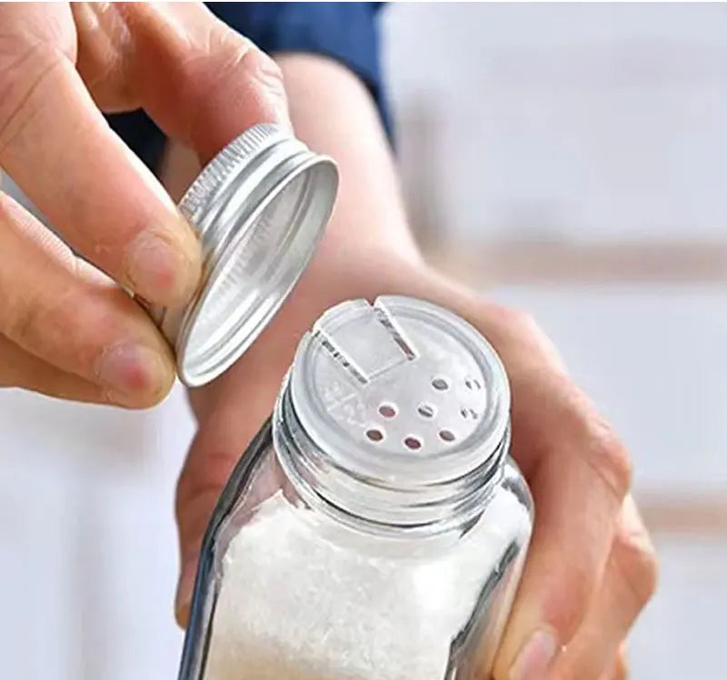Close-up of glass herb bottles with airtight metal caps and a sift-and-pour inner lid.