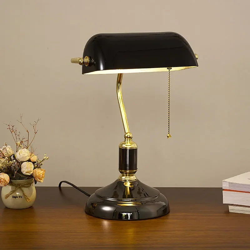 Black glass banker desk lamp with a gold-tone frame on a wooden tabletop