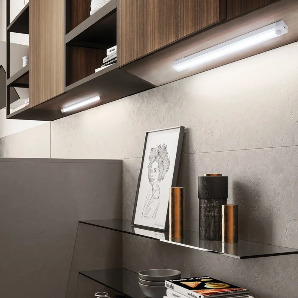 Modern kitchen setup with wooden cabinets, wall lights, and decorative items on a shelf.