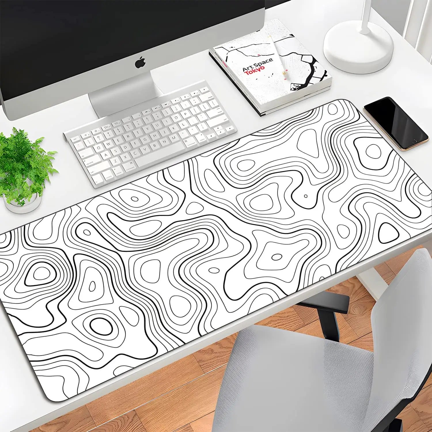Desk setup with a large desk mat featuring a black and white topographic design, keyboard, computer monitor, and phone.