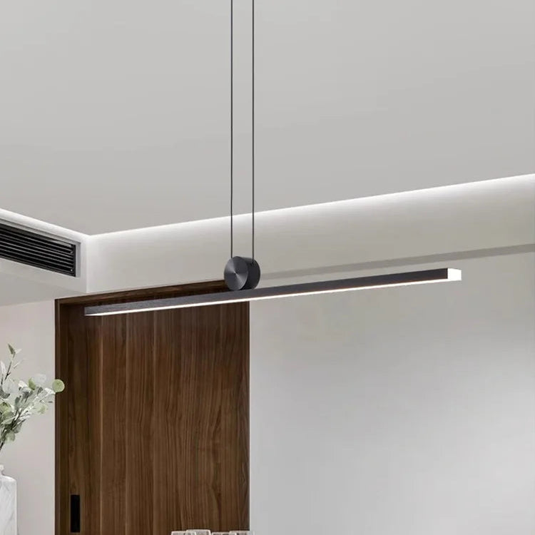 Modern dining area with a long pendant light fixture, white table, and black chairs.