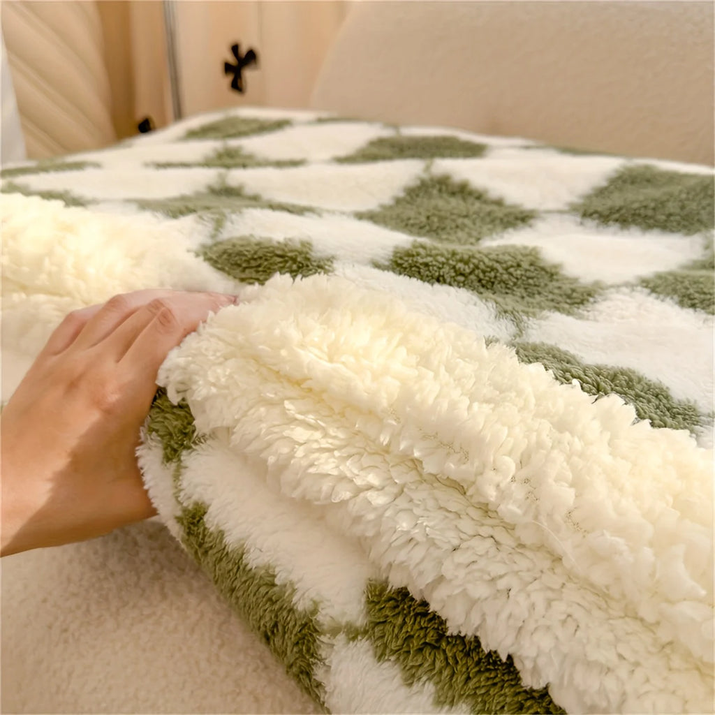 Green and white checkered blanket with a hand touching it, on a bed.