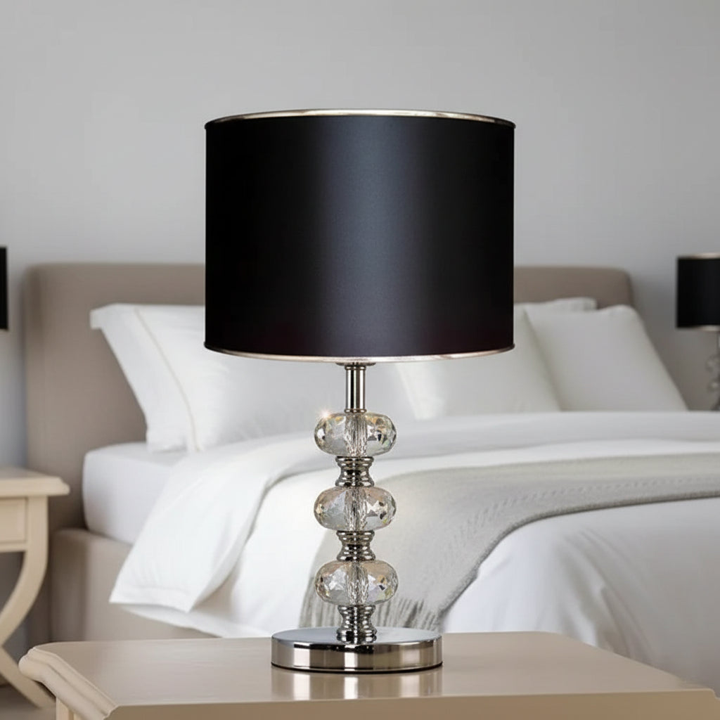 table lamp with a solid black cylindrical shade and a triple-stacked crystal base on a nightstand.