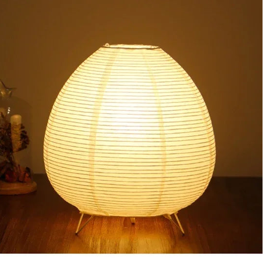 Round Japenese lamp on a wooden floor with a plant in the background