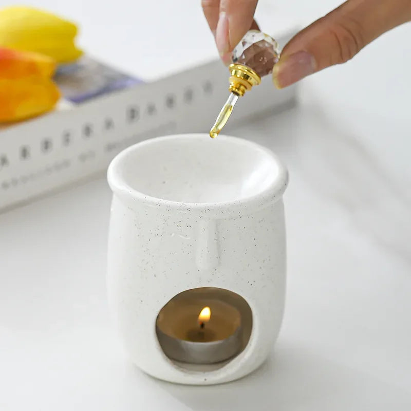 Person adding essential oil to a ceramic diffuser with a lit candle inside.