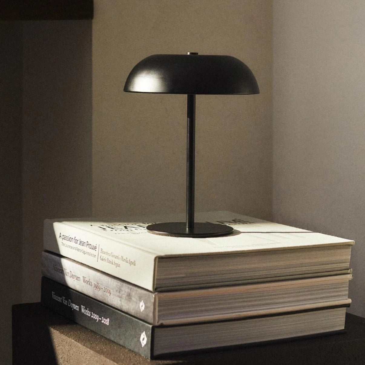 Black mushroom table lamp on a stack of books with a neutral background