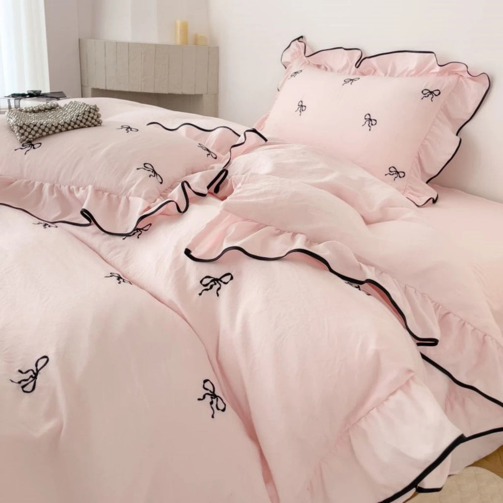 Wide shot of the Soft Blush duvet set on a bed, showcasing the repeating bow pattern and romantic ruffles in a bright, airy room.