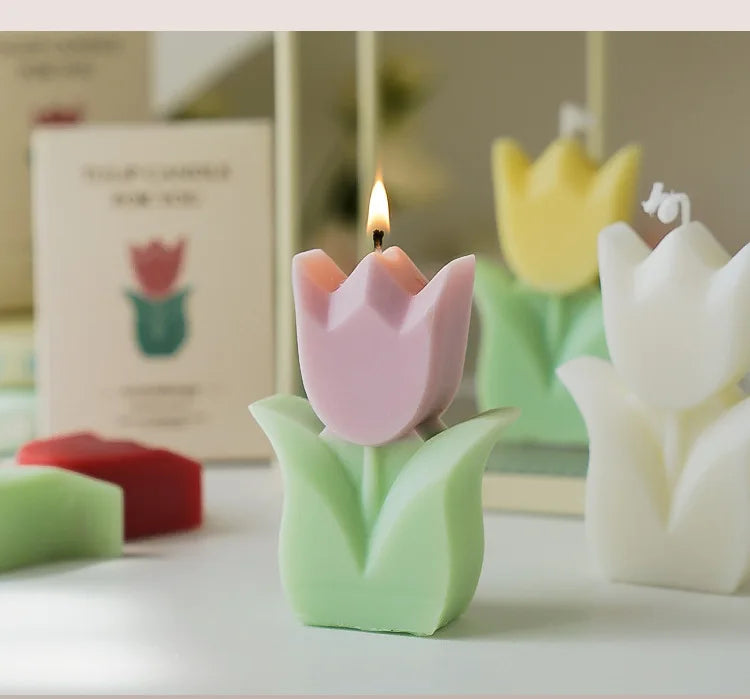 Pink tulip-shaped scented candle with a green base on a white surface, with a blurred background.