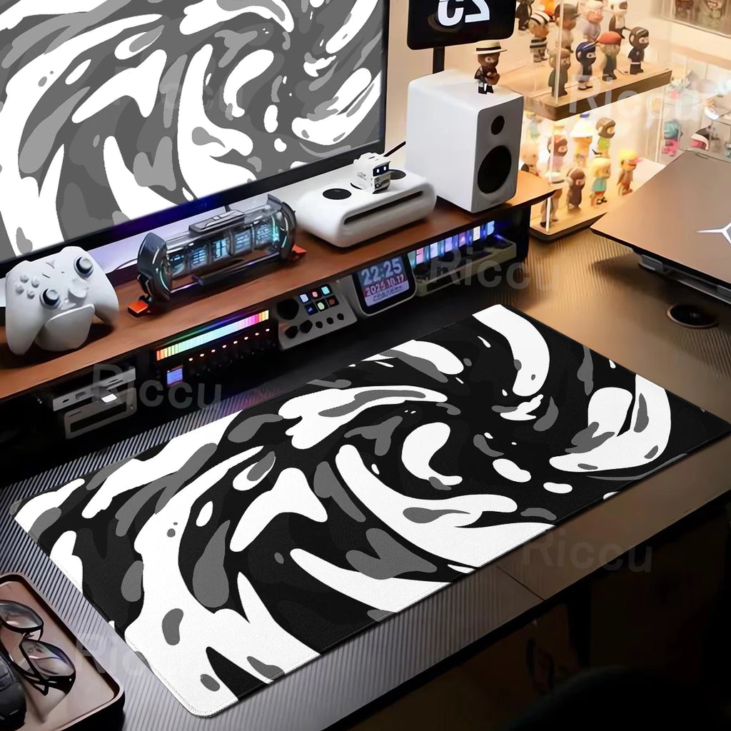 Gaming desk setup with a black and white patterned mouse pad, monitor, speakers, and other gaming accessories.