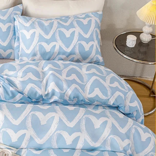 Blue and white heart-patterned bedding set on a bed with a side table in the background.