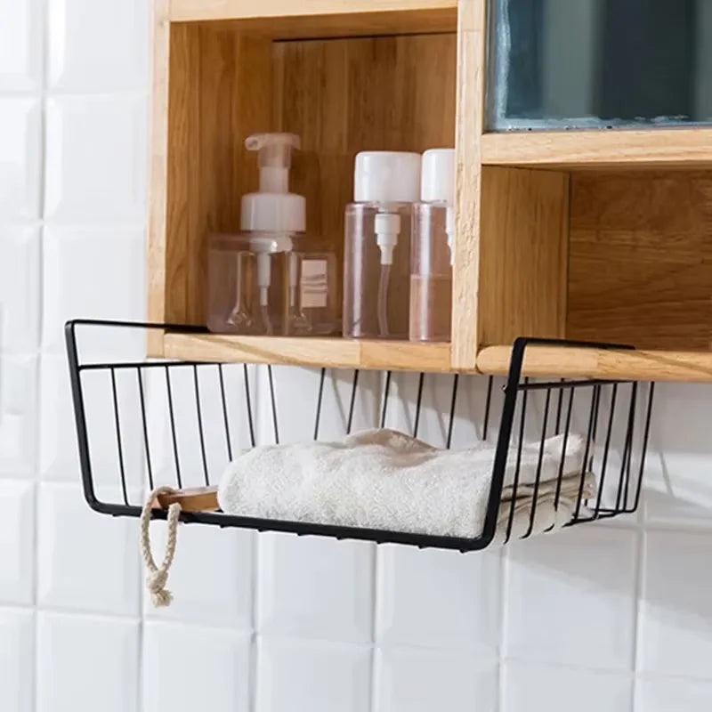 Black wire basket with a towel and soap on a wooden shelf against a white tiled wall.