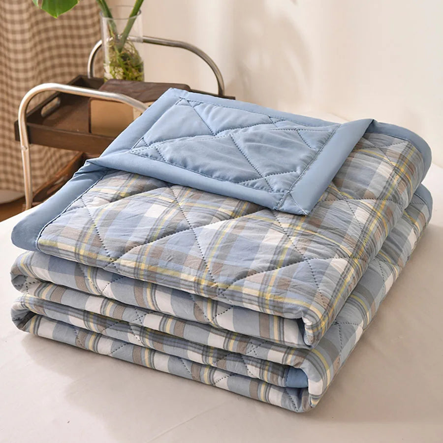 Light blue, lilac, and cream plaid quilted comforter folded on a bed with a blue border