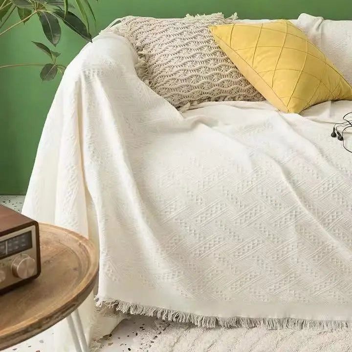 Bed with white comforter, yellow pillow, and textured grey throw blanket against a green wall.