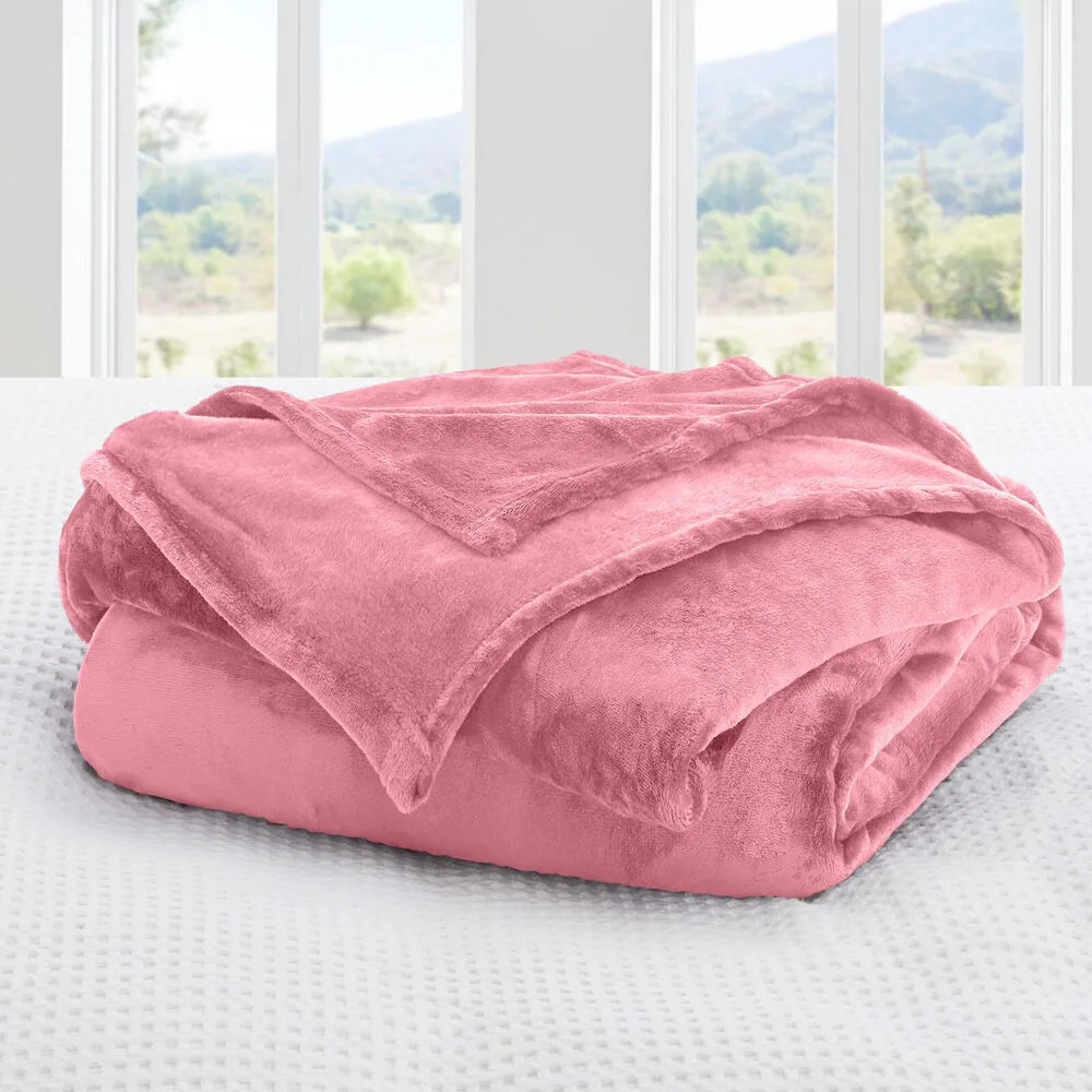 A blush Pink blanket on a bed with a window view of greenery