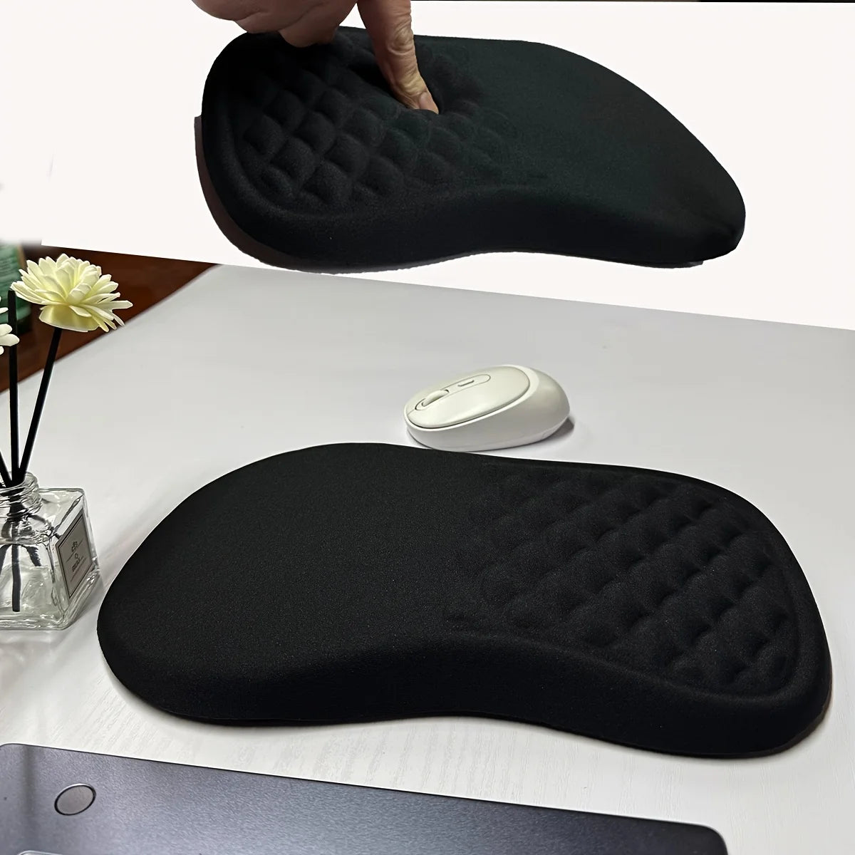 Black ergonomic mouse pad on a desk with a computer mouse and flowers.