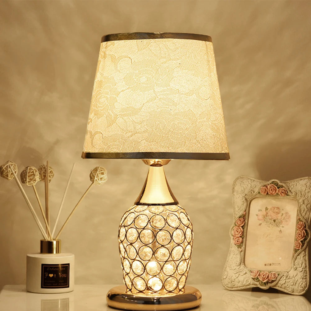 Gold crystal-lattice bedside lamp with gold scrollwork fabric shade on a nightstand.