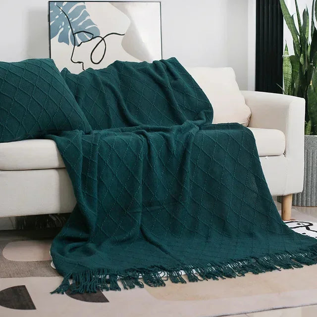 Dark green textured knit throw with fringed ends falling over a cream sofa with a matching cushion