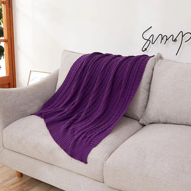 Purple blanket draped over a gray sofa with a visible brand logo in the corner.