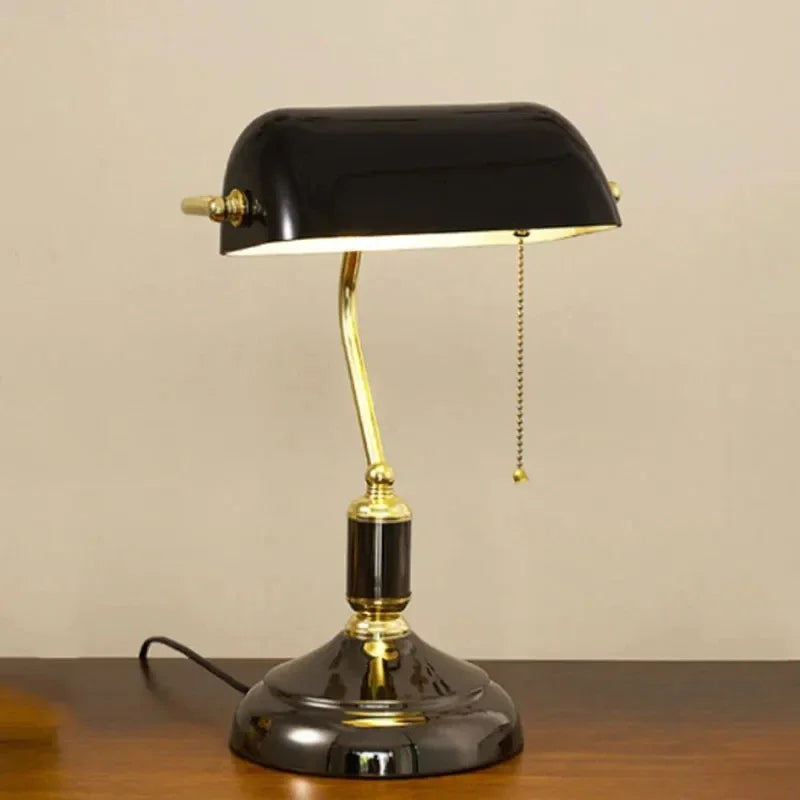 Black glass banker desk lamp with a gold-tone frame on a wooden tabletop