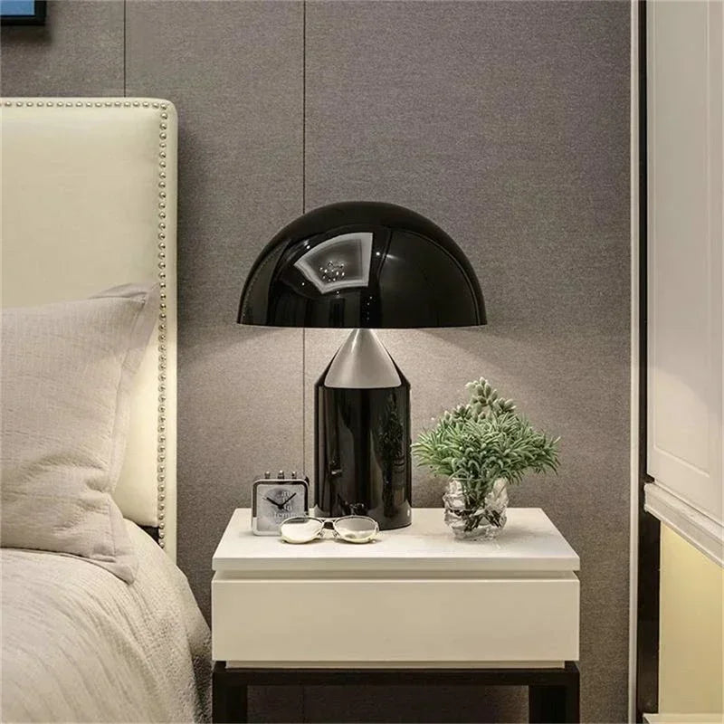 Modern bedroom with a nightstand, lamp, clock, and small plant against a gray wall.
