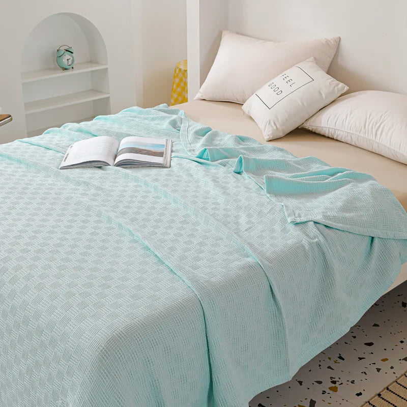 A mint-textured blanket on a bed with pillows and an open book.