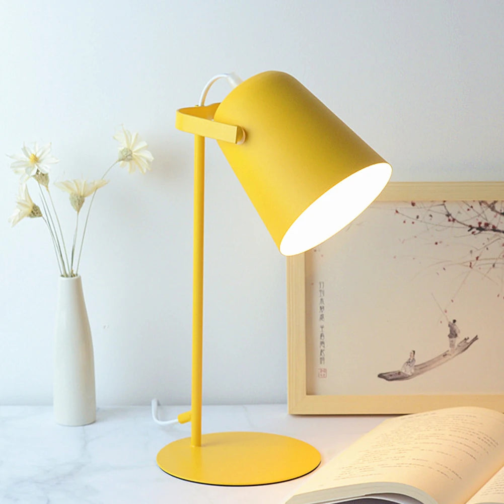 Yellow desk lamp on a table with a vase and framed picture in the background