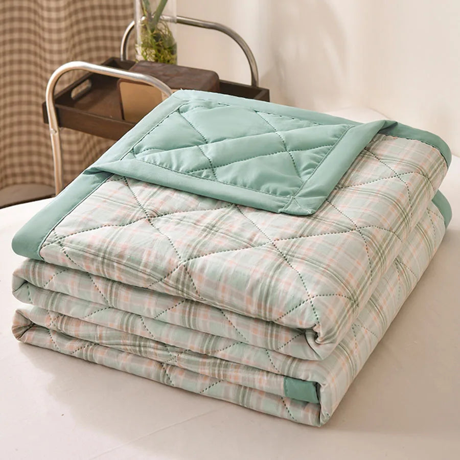 Mint green plaid quilted comforter with peach accents and a mint border, folded on a bed
